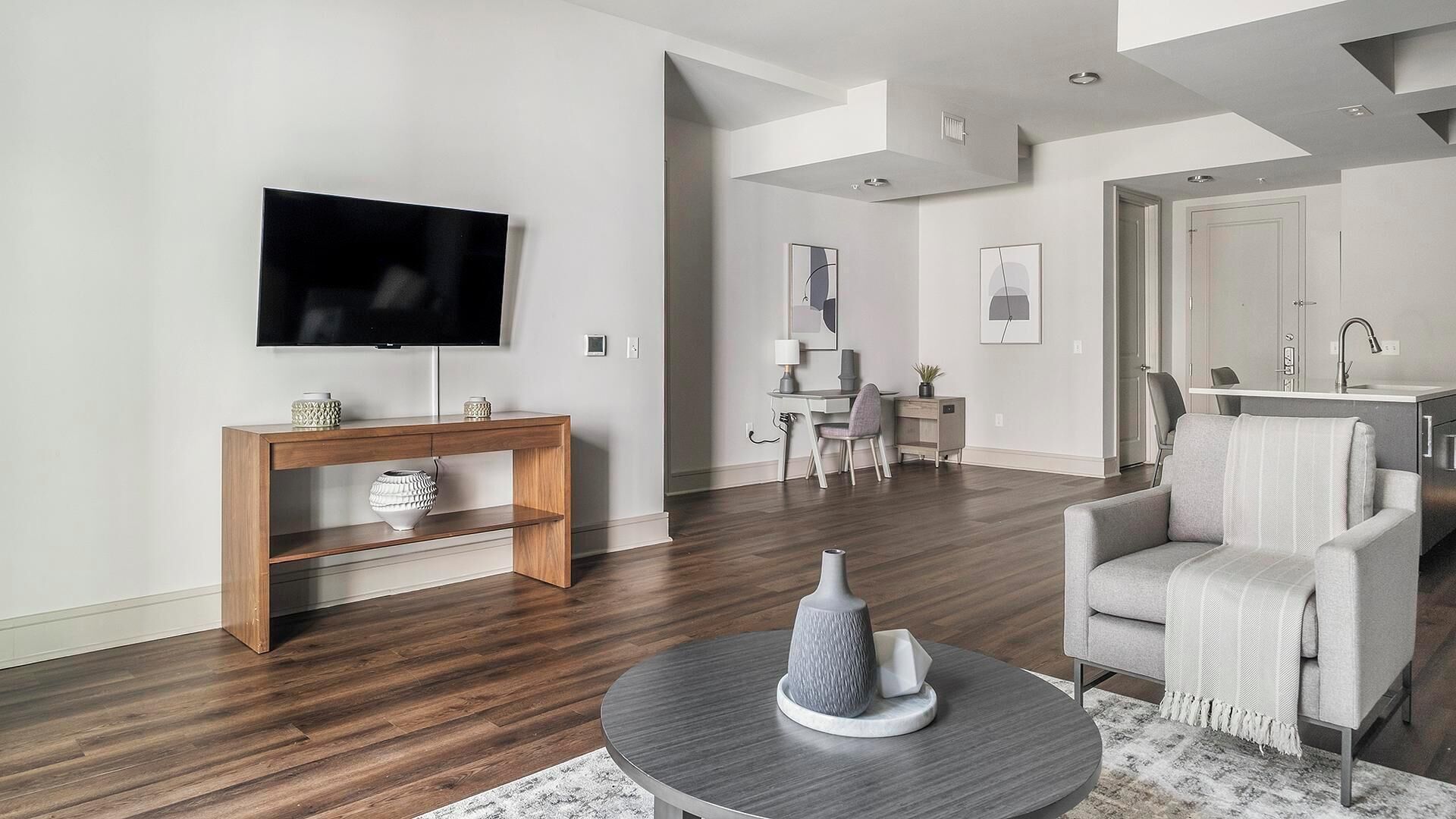 Un salon moderne avec un téléviseur à écran plat, une console en bois, un canapé gris et une table basse ronde.