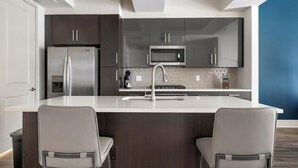 A modern kitchen with dark wood cabinets, stainless steel appliances, and a central island with two chairs.