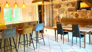 A rustic interior with exposed wooden beams, a stone wall, and a bar area with stools and a table. - QUINTA DE RIBAS - LA CLEF DES CHAMPS - AUTHENTIC LITTLE HOUSE (Vila cha do marao, amarante)