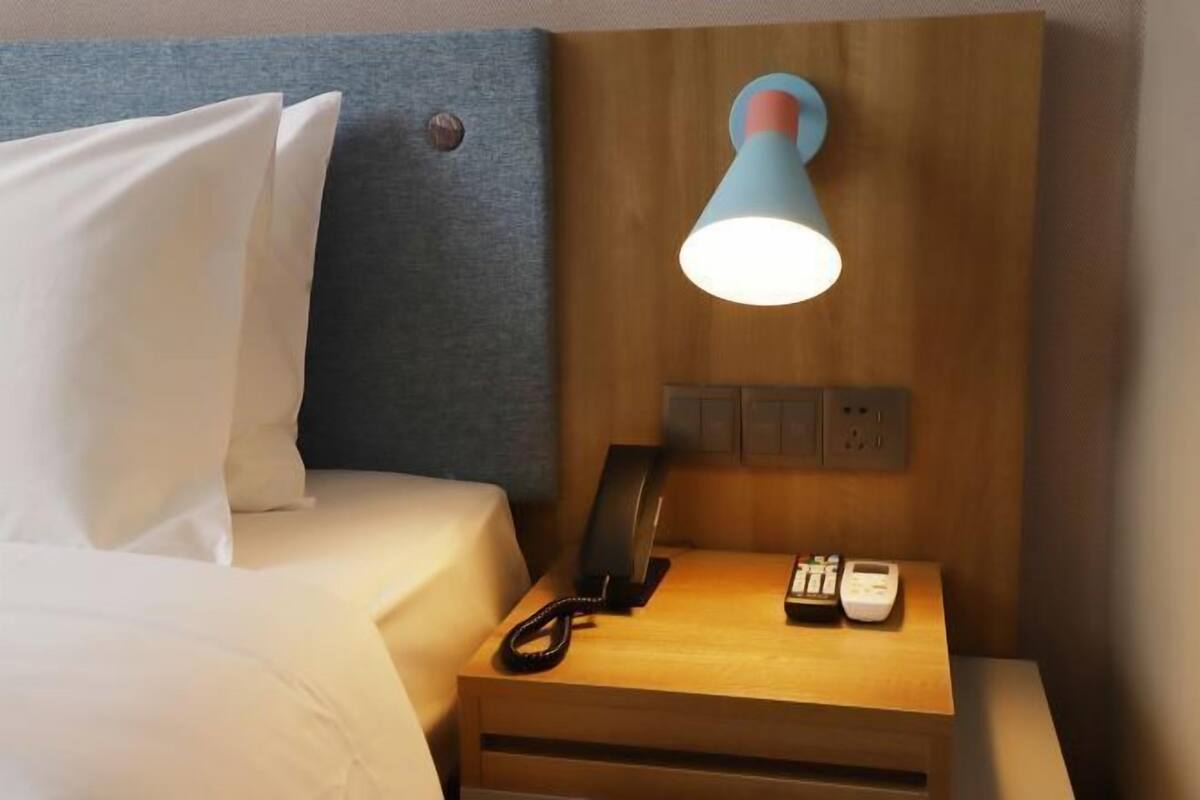 A hotel room with a bed, a bedside table with a lamp, a phone, and a power outlet.