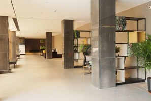 Un hall espacioso con techos altos, una recepción, zonas de estar y un mueble de almacenamiento moderno con plantas.
