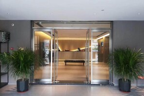 Un vestíbulo de hotel con una recepción, un banco y dos plantas en macetas.