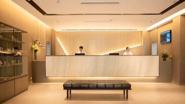 A modern reception area with a reception desk, two staff members, a bench, and a glass display cabinet. - Homeinn · neo (Qufu Jingxuan Middle Road Sankong) (Qufu)