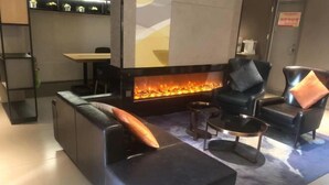 A modern living room with a black leather sofa, two black armchairs, a coffee table, and a fireplace with a visible fire. - Homeinn · neo (Qufu Jingxuan Middle Road Sankong) (Qufu)