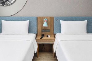 A hotel room with two beds, a wooden headboard, a nightstand, a lamp, and a telephone.