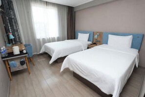 A hotel room with two beds, a desk with a chair, a lamp, and a window with curtains.