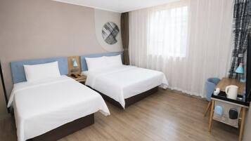 Una habitación de hotel con dos camas, un reloj de pared redondo, una mesita con lámpara y una ventana con cortinas.