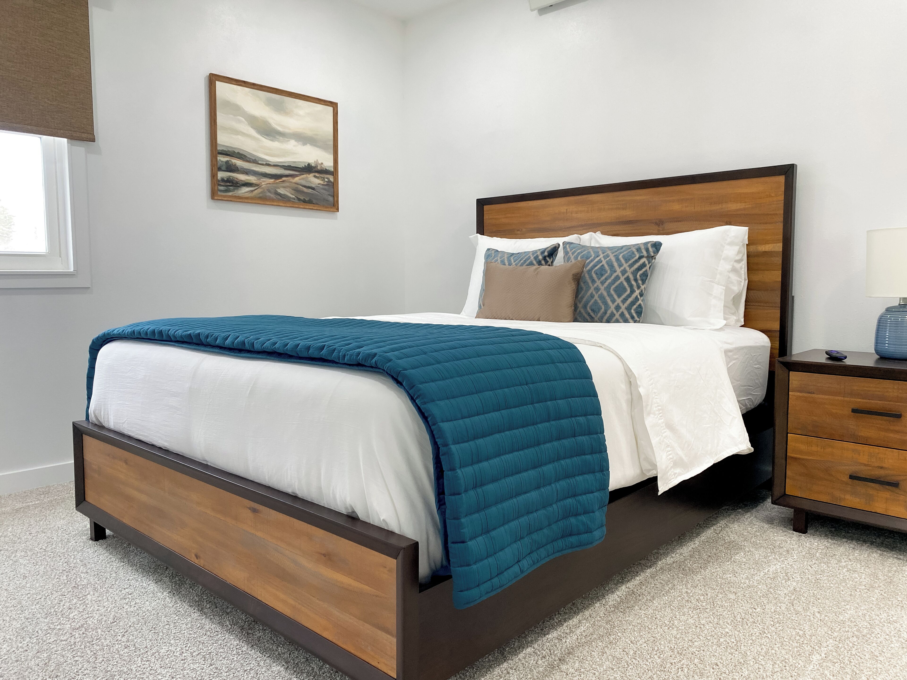 A bedroom with a bed, a nightstand, a lamp, and a painting on the wall.