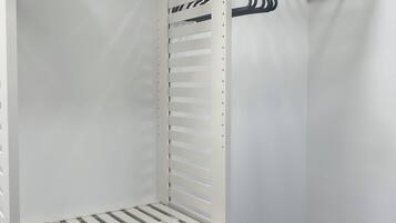 Un armari blanc amb diverses prestatgeries i espai penjador, un calaix petit i una barra metàl·lica per penjar coses.