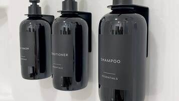 Trois flacons noirs de shampoing et d’après-shampoing sont fixés à un mur blanc.