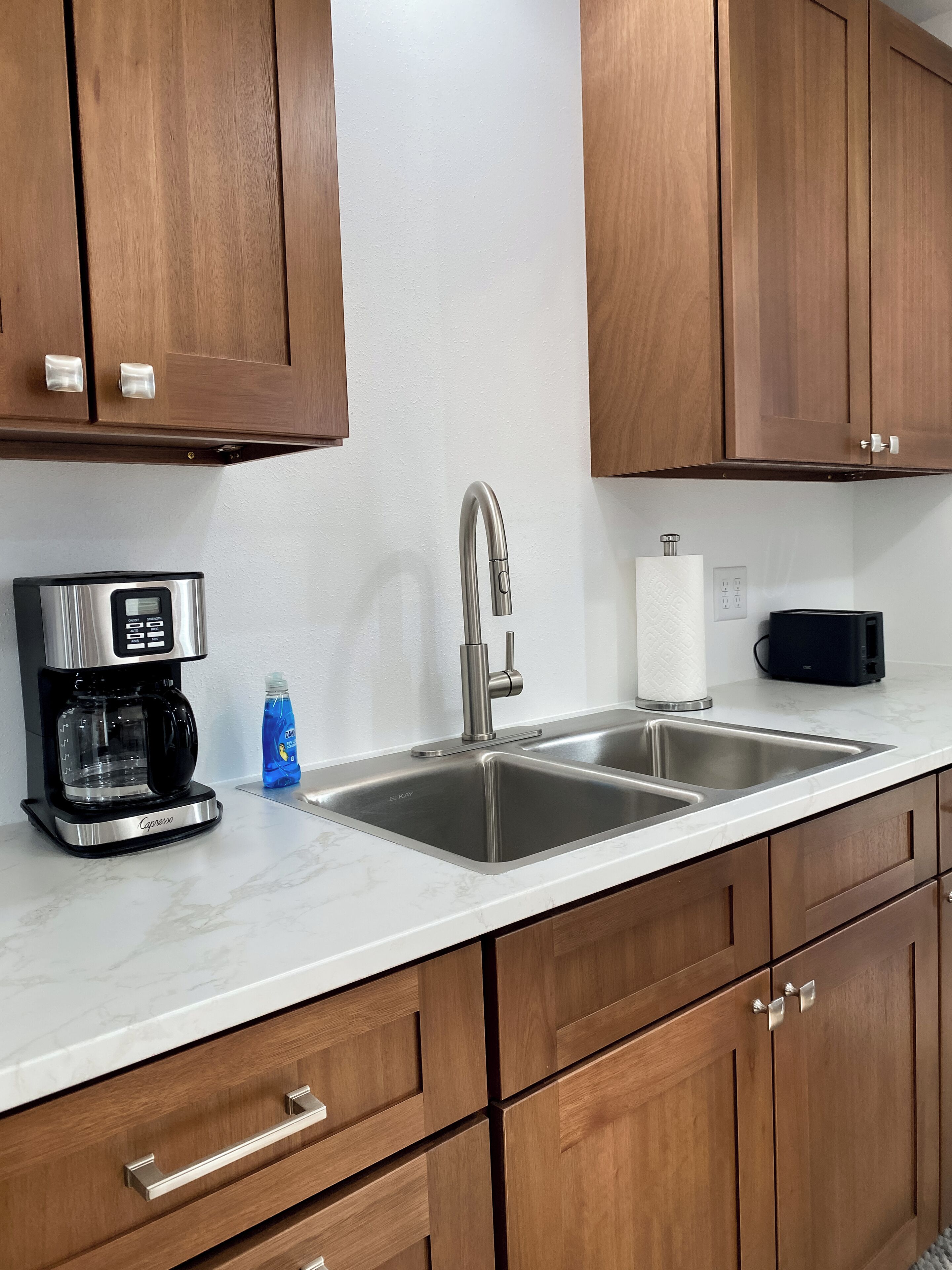 A kitchen with wooden cabinets, a stainless steel sink, a coffee maker, and a bottle of dish soap.