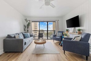 A modern living room with a sofa, armchair, round coffee table, and a TV mounted on the wall. - The Coral Cove in Myrtle Beach (Myrtle Beach)
