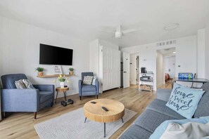 A modern living room with a grey sofa, a round coffee table, and a flat-screen TV mounted on the wall. - The Coral Cove in Myrtle Beach (Myrtle Beach)
