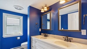 Een badkamer met twee wasbakken, een toilet en een raam met zonwering.