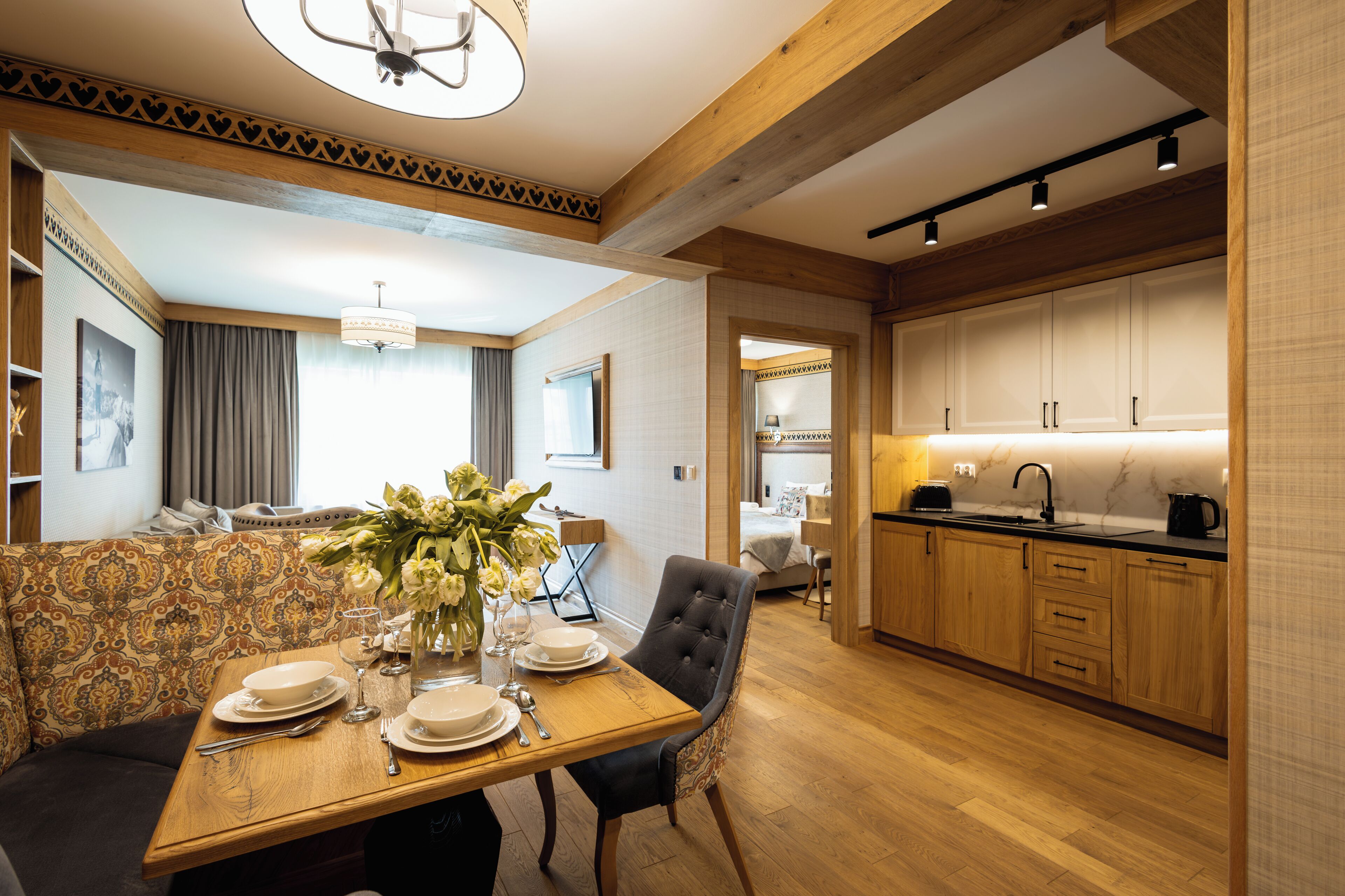 A modern kitchen with wooden cabinets, a dining area with a table set for four, and a living area with a sofa and a decorative vase.