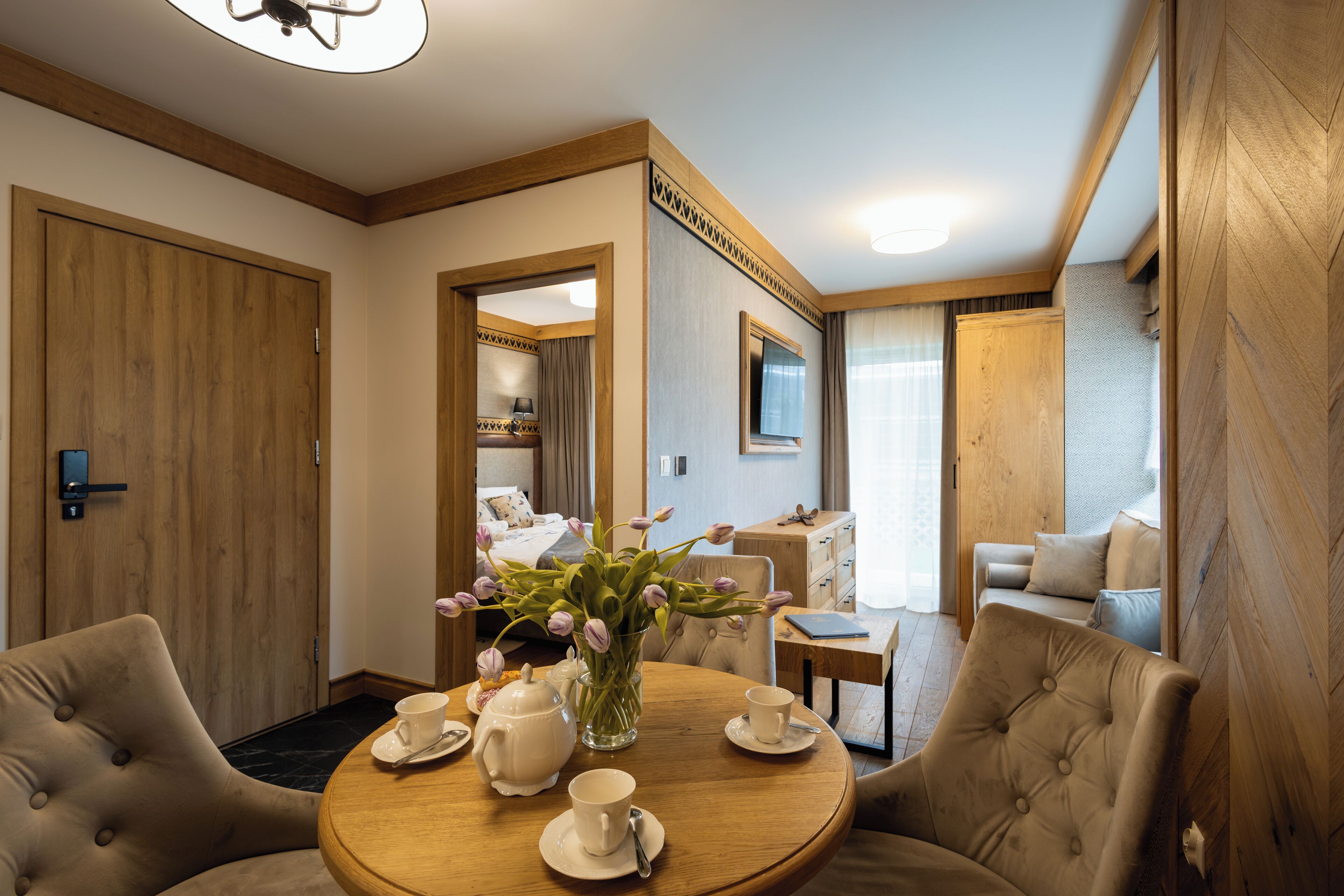 A hotel room with a round dining table set for four, a vase of flowers, and a bed in the background.