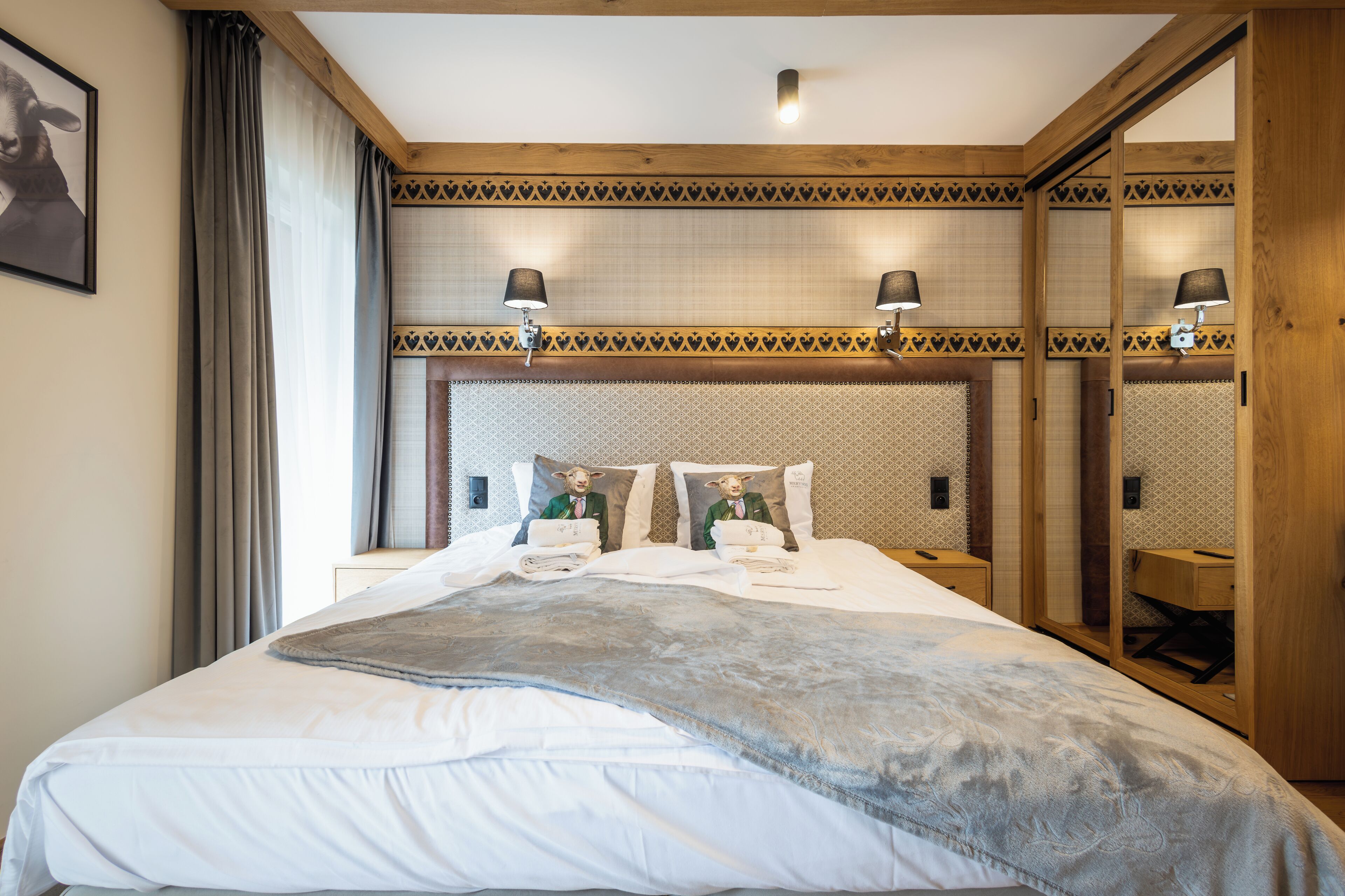 A neatly made bed with a gray blanket, a wooden headboard with patterned cushions, and two bedside lamps.
