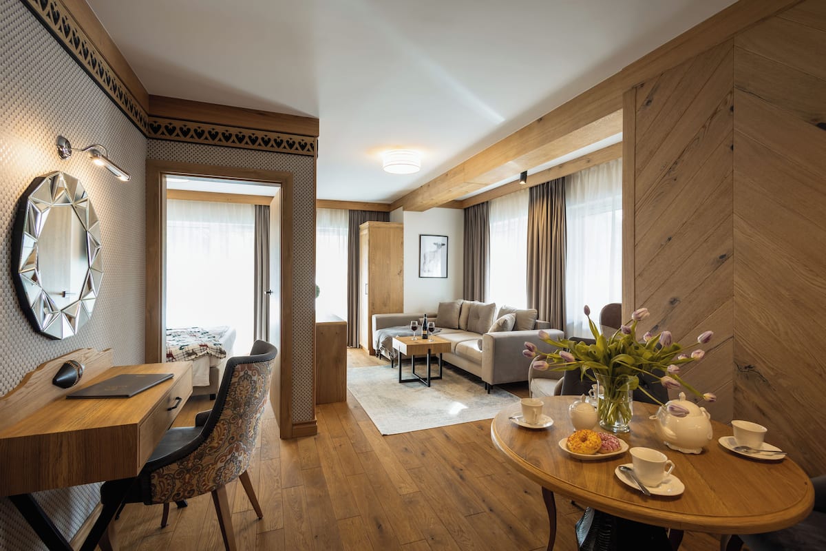 A modern hotel room with a wooden desk, a comfortable sofa, a dining table with tea set, and a large mirror.