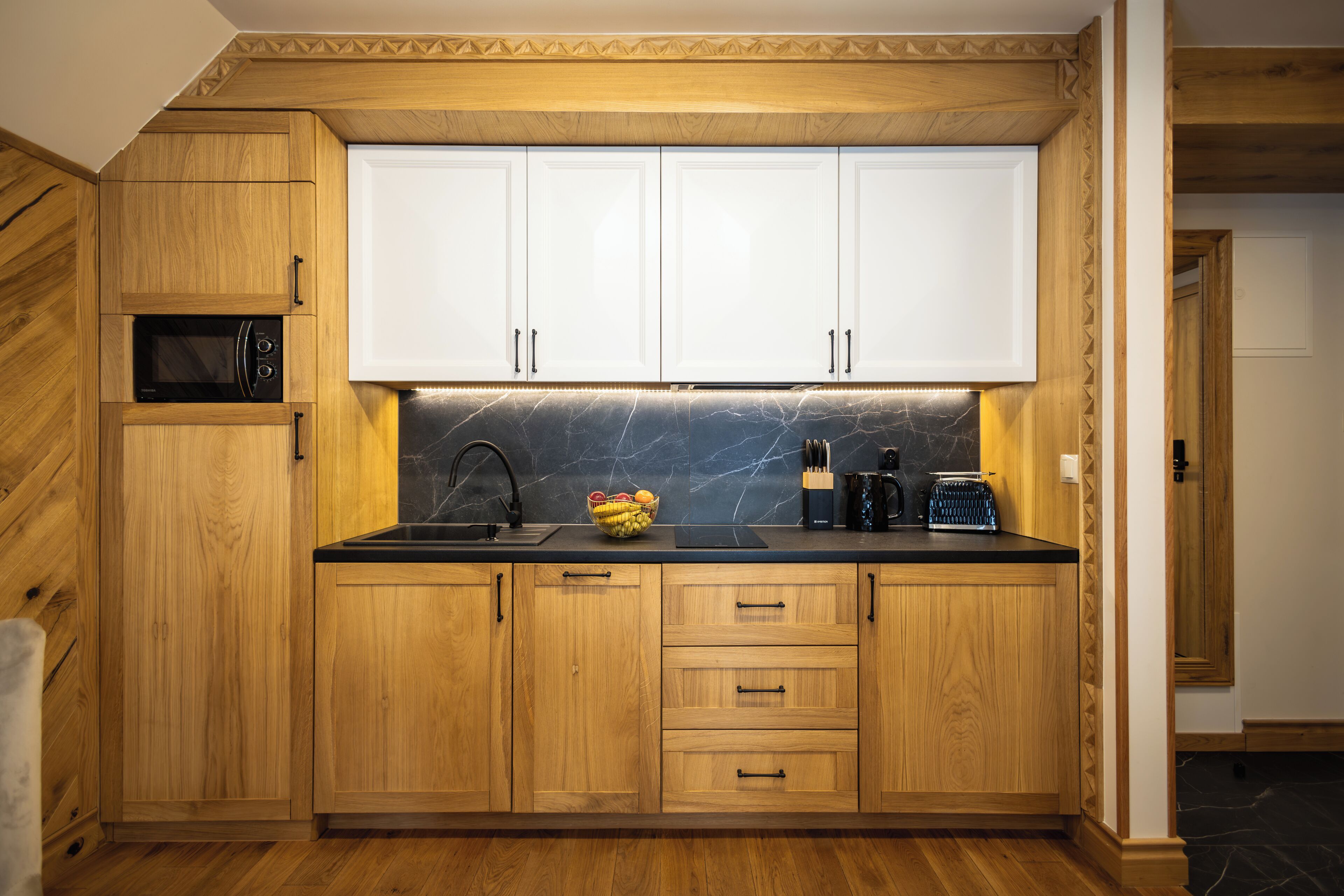 A compact kitchen with wooden cabinets, a built-in microwave, and a marble backsplash.