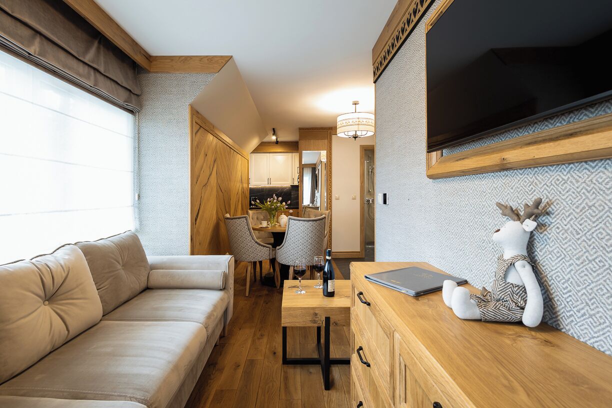 A cozy living area with a sofa, dining table, and a wooden cabinet with a laptop and a stuffed animal.