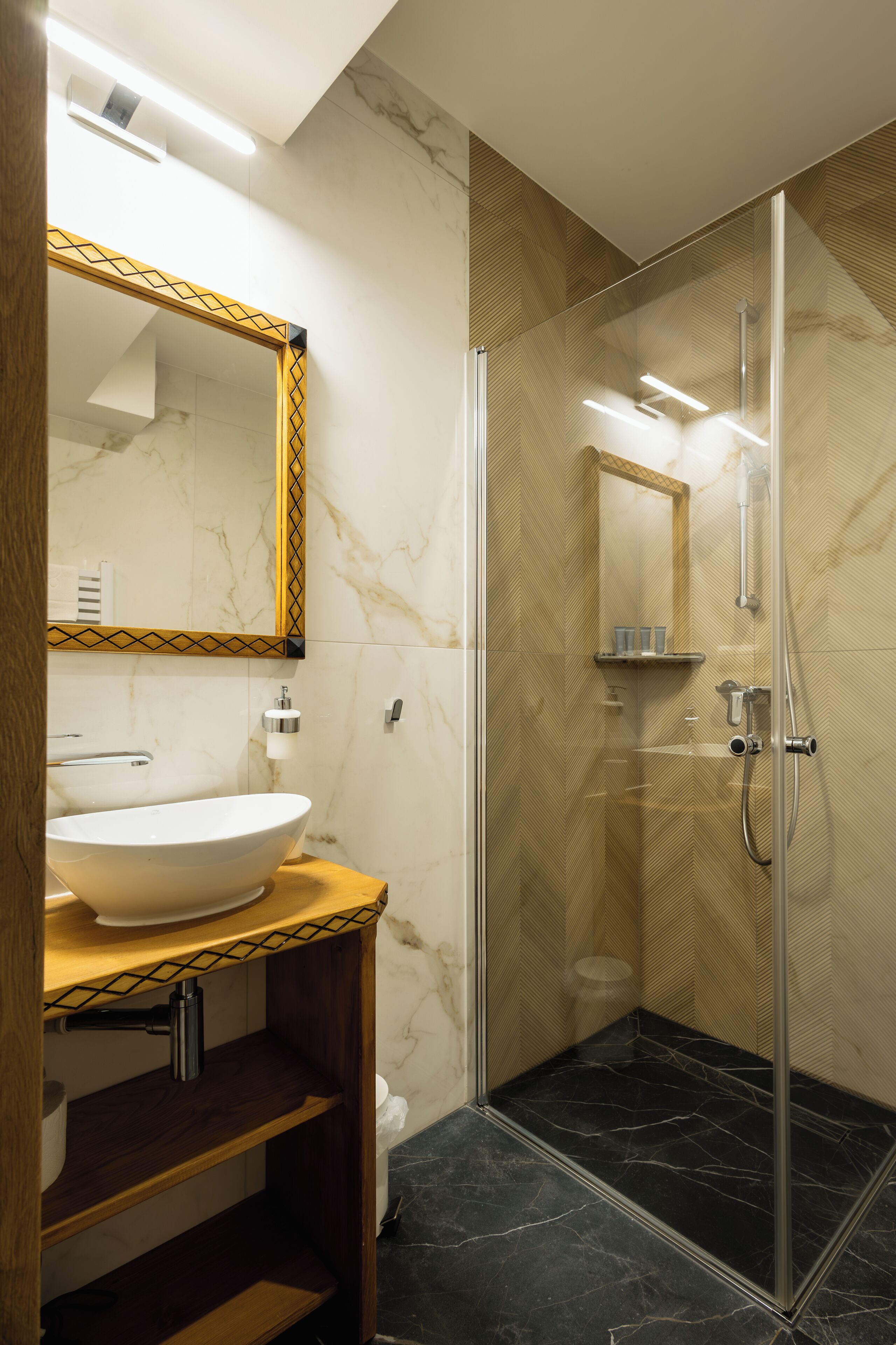 A modern bathroom with a large mirror, a vessel sink, a shower enclosure, and marble walls.