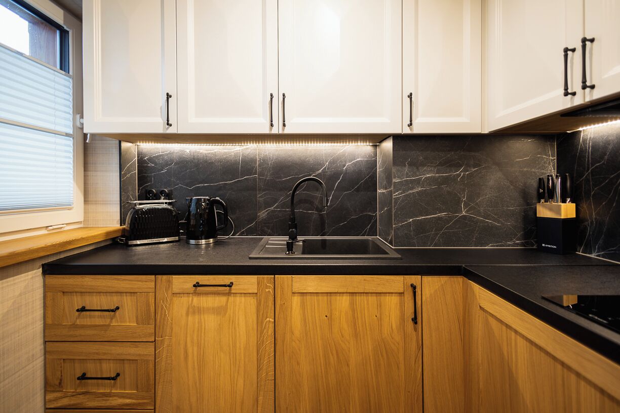 Una cucina moderna con mobili bianchi, una schiena di marmo nero e cassetti in legno.
