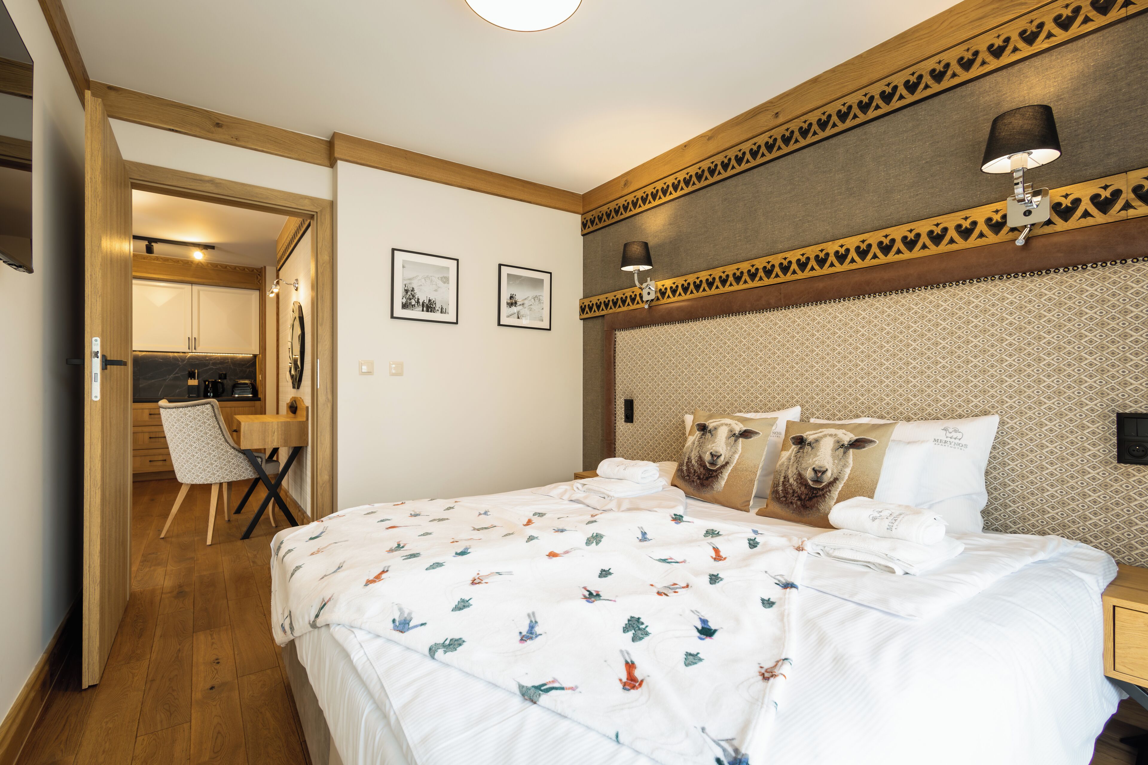 A hotel room with a bed, a desk, and a chair. There are two framed pictures on the wall.