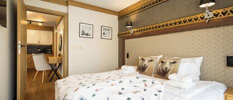 A hotel room with a bed, a desk, and a chair. There are two framed pictures on the wall.