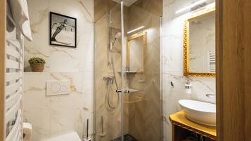 Un baño moderno con ducha de vidrio, lavamanos blanco y pared de mármol.