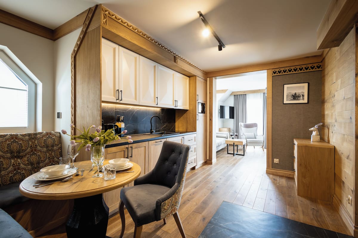 A modern kitchen with wooden cabinets, a dining area with a round table and chairs, and a view into the living room.