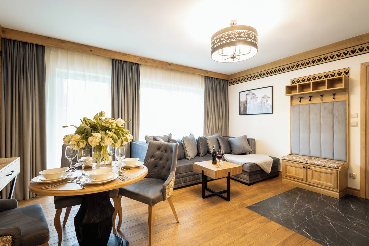 A modern living room with a dining area, wooden furniture, and a large window with curtains.