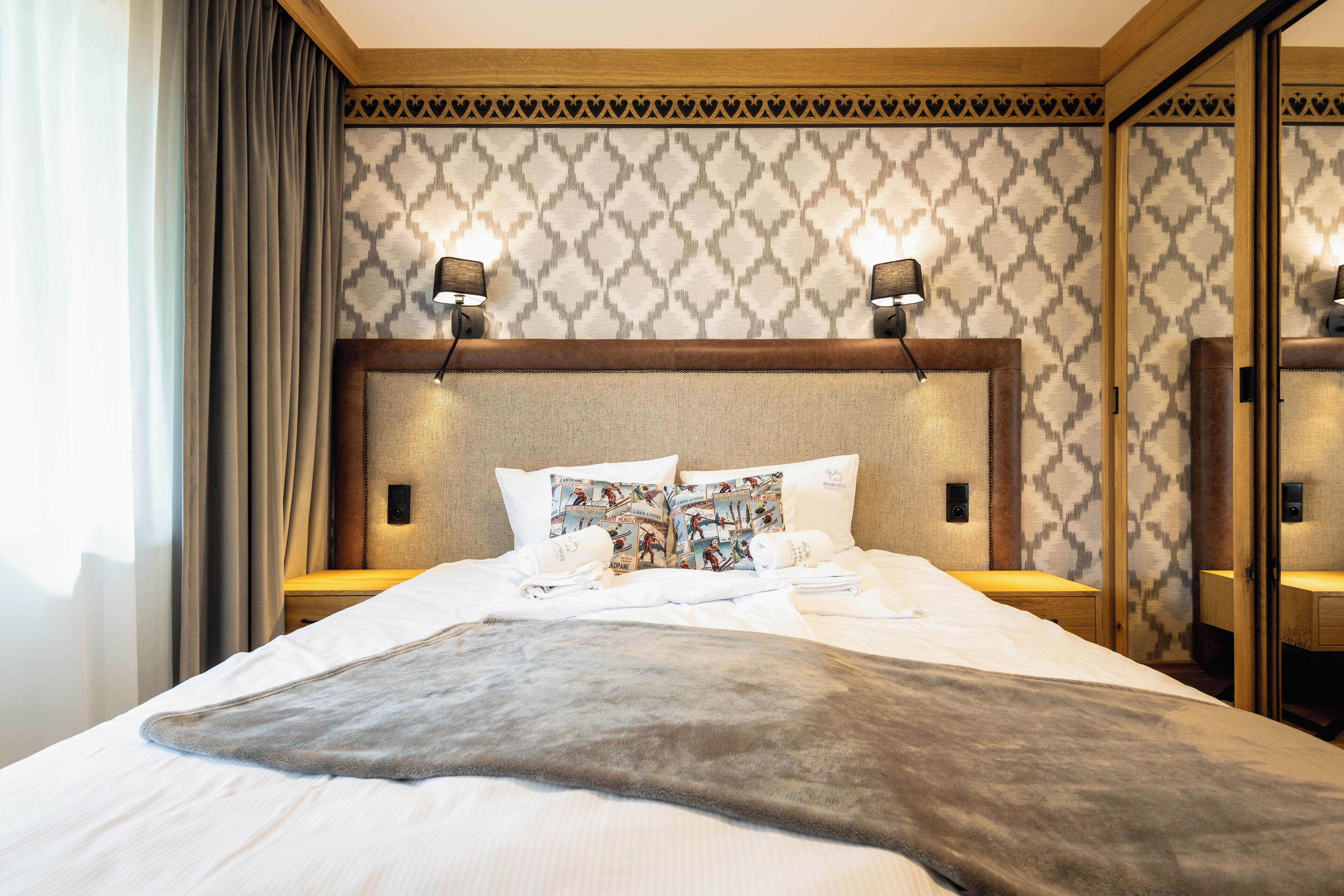A neatly made bed with a grey blanket, two bedside lamps, and patterned wall decor.