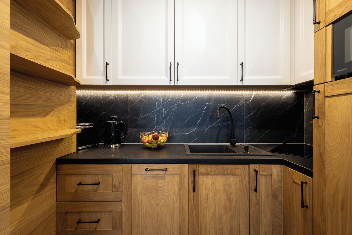 Een keuken met houten kastjes, een zwart aanrecht, een spoelbak en een fruitschaal.