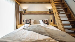 A bedroom with a bed, nightstands, a patterned headboard, a wooden staircase, and a window with curtains. - Aparthotel Merynos (Zakopane)
