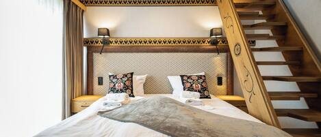 A bedroom with a bed, nightstands, a patterned headboard, a wooden staircase, and a window with curtains.