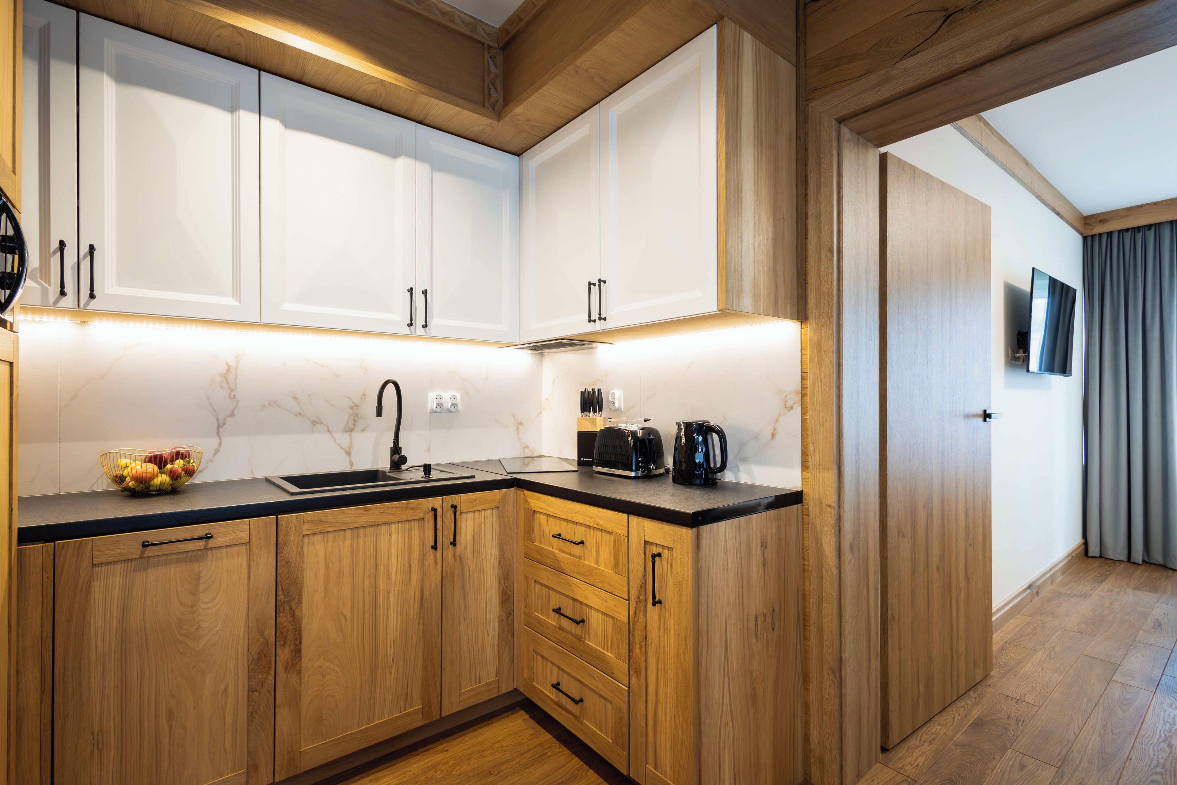 A modern kitchen with wooden cabinets, a black countertop, and a fruit bowl.