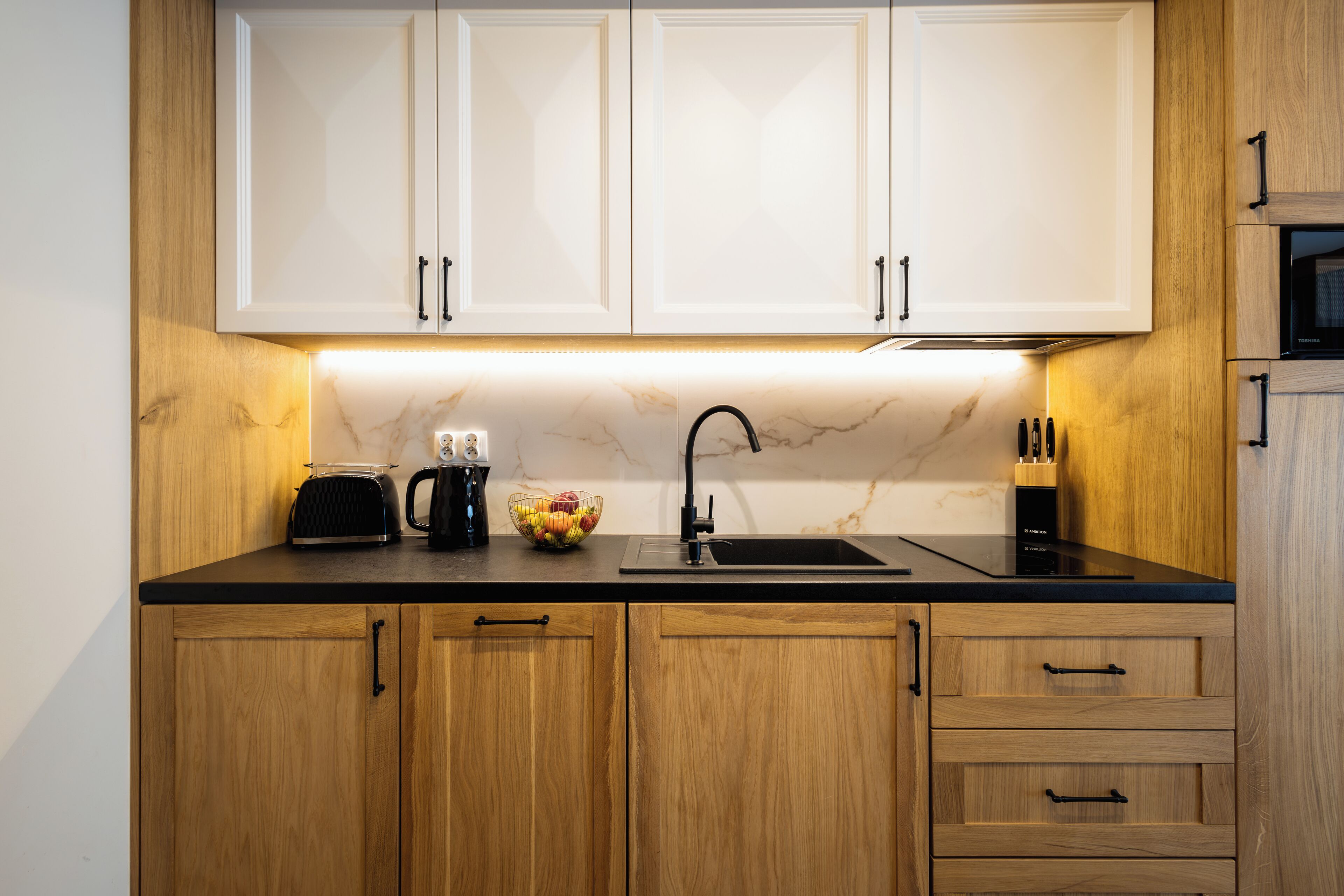 A kitchen with wooden cabinets, a black countertop, a sink, and a microwave.