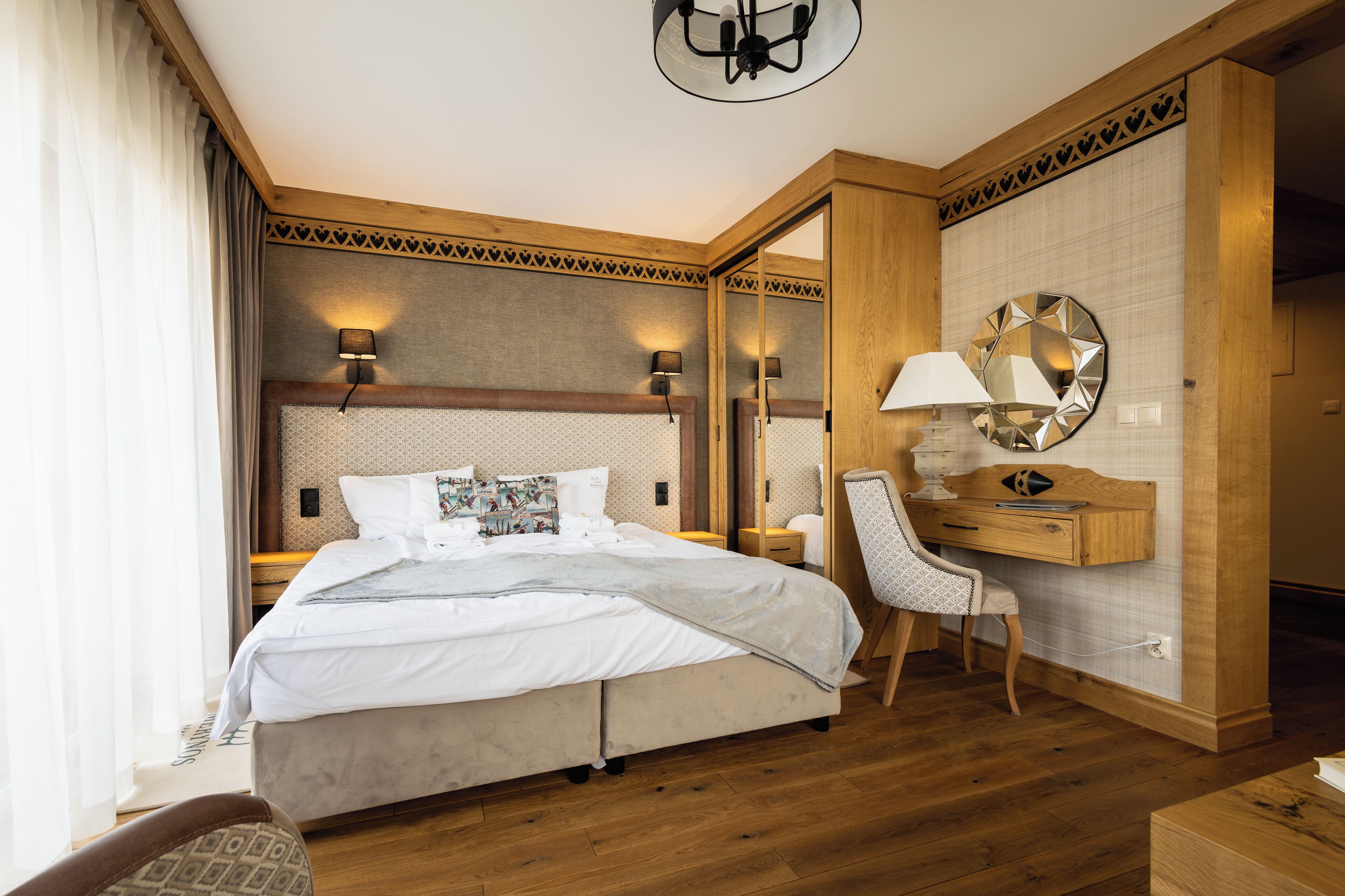 A hotel room with a large bed, a desk, a chair, and a mirror.