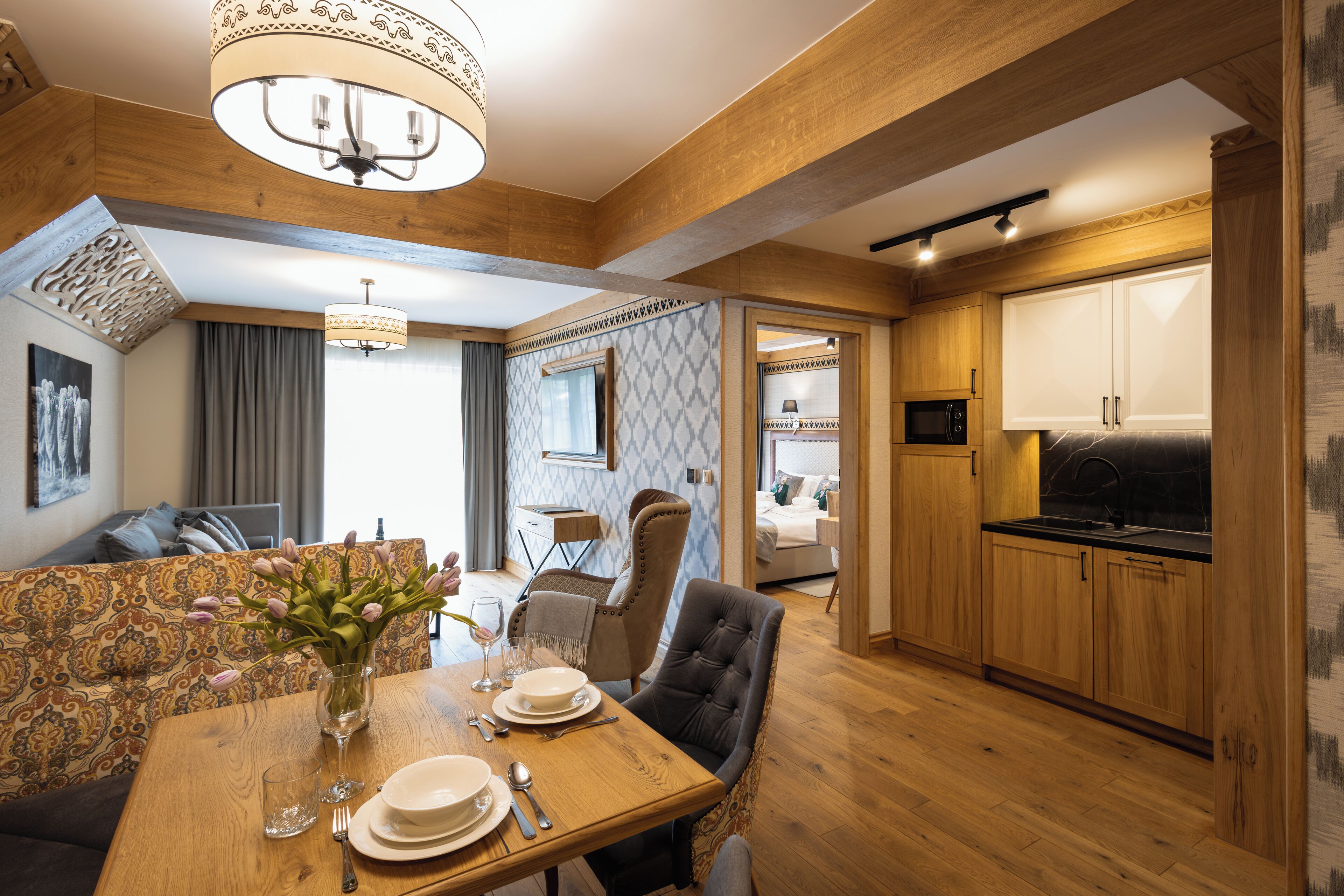 Zona pranzo con tavolo in legno apparecchiato per quattro persone, un vaso con fiori e un lampadario.