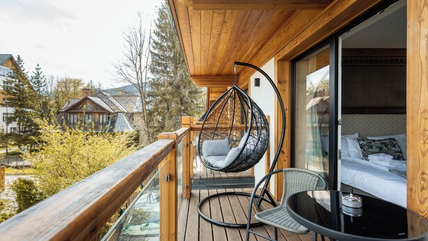 A wooden deck with a hanging chair and a table, overlooking a residential area with houses and trees. - Aparthotel Merynos (Zakopane)