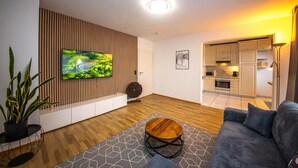 Ein modernes Wohnzimmer mit Fernseher, einer Wand aus Holzpaneelen, einem Essbereich und einer Küche.