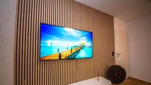 Ein Flachbildfernseher an einer Wand aus Holzleisten, mit Holzboden und einer weißen Konsole darunter.