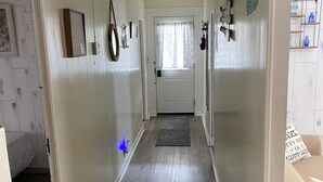 Un couloir avec un plancher en bois, des murs blancs et une porte au fond.