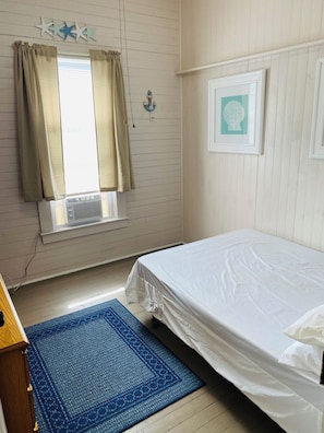 Ein Schlafzimmer mit Bett, einem fenster mit Vorhängen, einer Klimaanlage, einem blauen Teppich und einer Wanddekoration.