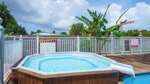 Ein Whirlpool auf einer Holzterrasse mit einem weißen Zaun und einem Pool im Hintergrund.