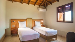 Ein Zimmer mit zwei Einzelbetten, Holz-Kopfteilen, einem Deckenventilator, einer Klimaanlage und einem Fenster mit Jalousien.