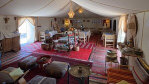 Een tentverblijf met een eetgedeelte, tafels en diverse zitmogelijkheden.