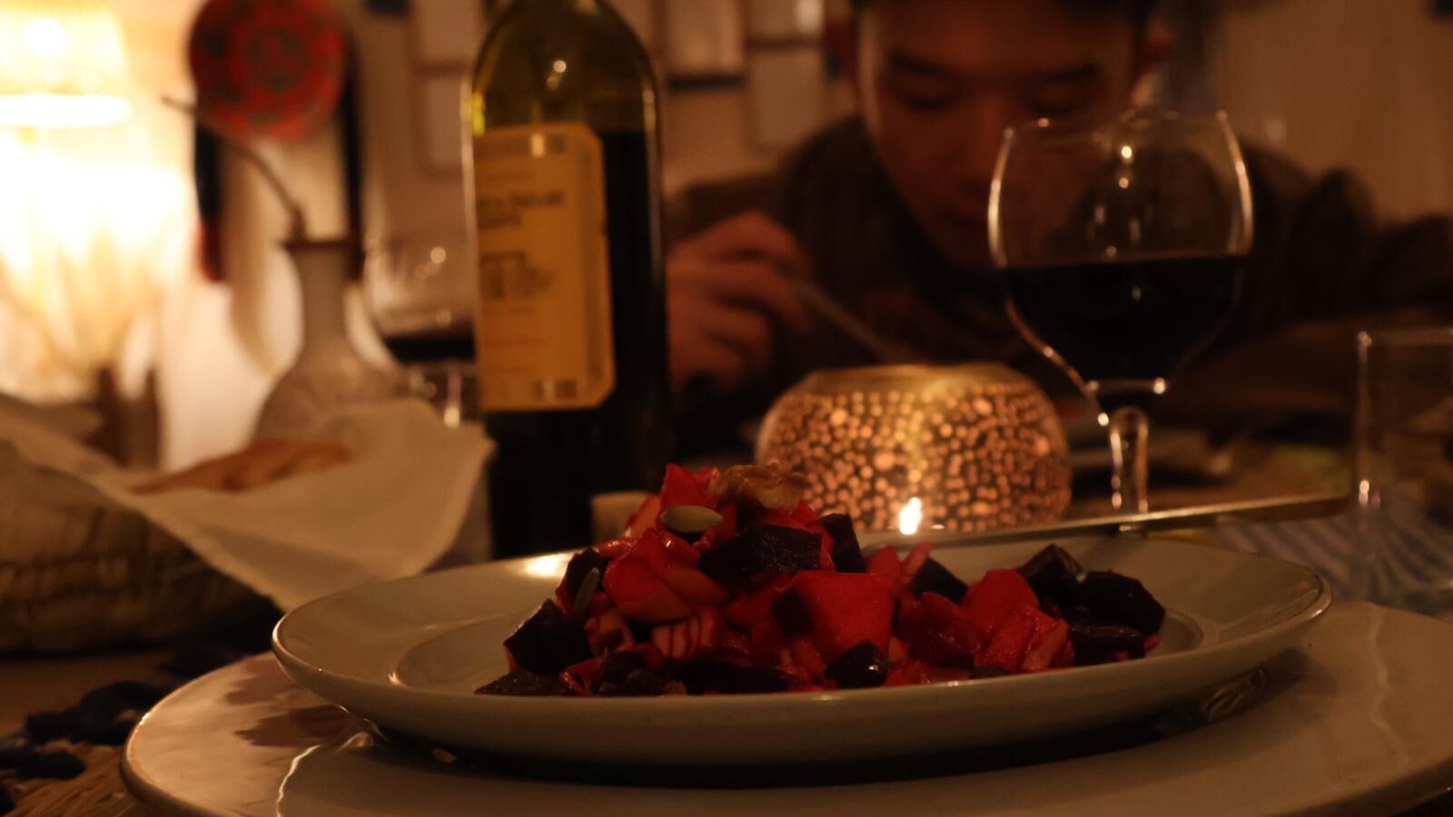 Un comedor tenuemente iluminado con una vela sobre la mesa, una botella de vino y un plato de comida.