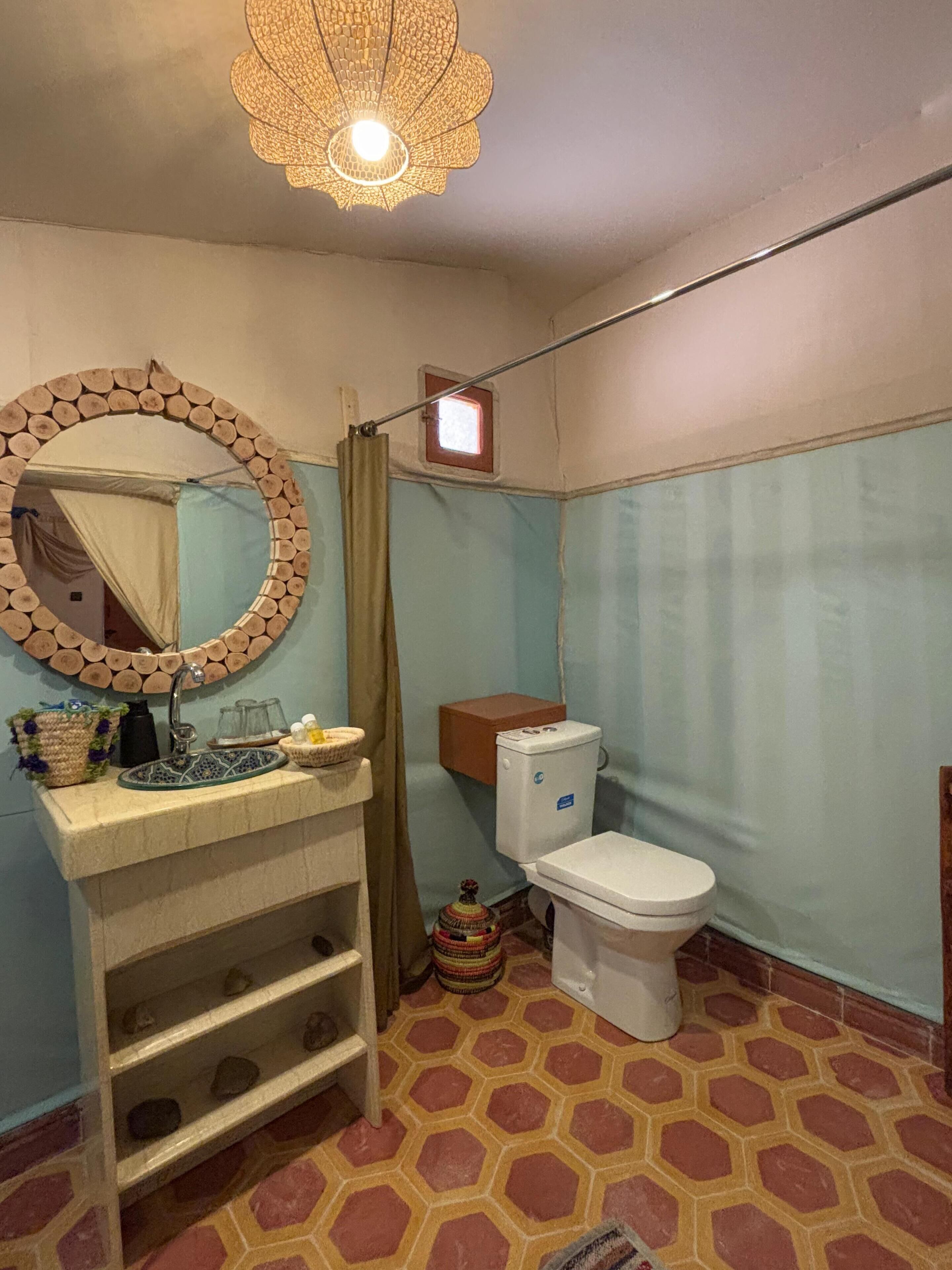 A bathroom with a wooden-framed mirror, a sink with a decorative basin, a toilet, and a shower curtain.