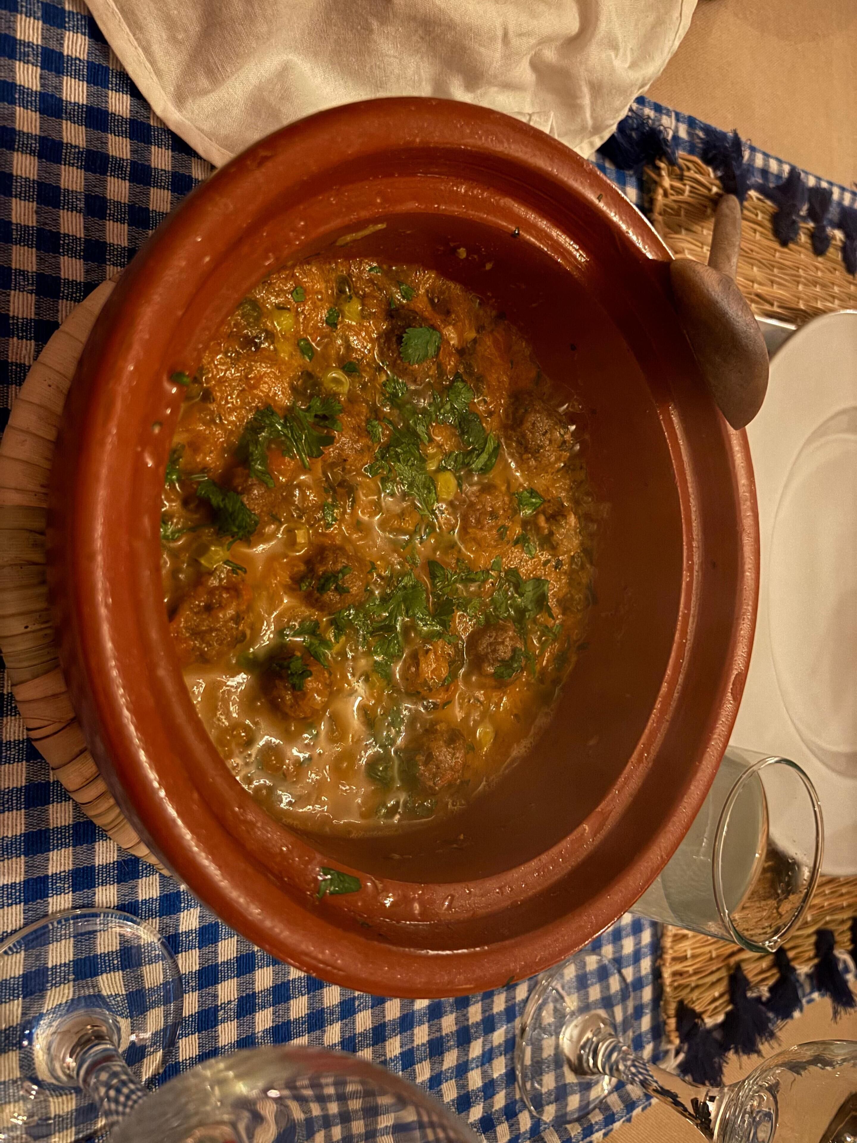 Una olla de barro llena de un guiso, sobre un mantel a cuadros.